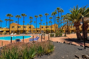 A resort with a swimming pool, palm trees, and yellow buildings. - GuestReady - Modern Stay with Pool and Terrace (Corralejo)