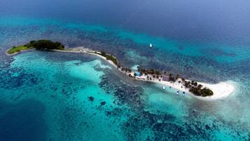 An aerial view of a tropical island with a beach, boats, and clear blue waters.