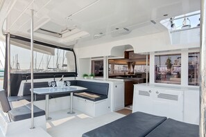 A boat interior with a dining area, seating, a kitchen, and a view of the marina. - Sun-Kissed Sailing Adventure in Islas Sarónicas (Alimos)