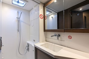 A modern bathroom with a shower, sink, and mirror. - Sun-Kissed Sailing Adventure in Islas Sarónicas (Alimos)
