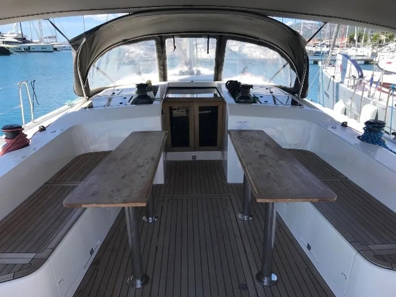 Um convés de barco com uma mesa central e dois bancos, rodeado por um soalho de madeira e um toldo.
