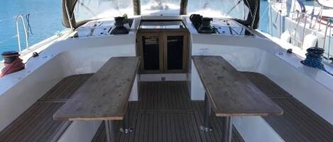 A boat deck with a central table and two benches, surrounded by a wooden floor and a canopy overhead.