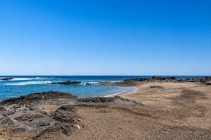 A coastal landscape with a rocky shoreline, a sandy beach, and a clear blue sky. - GuestReady - Bergantín Bañaderos Sea View (Arucas)
