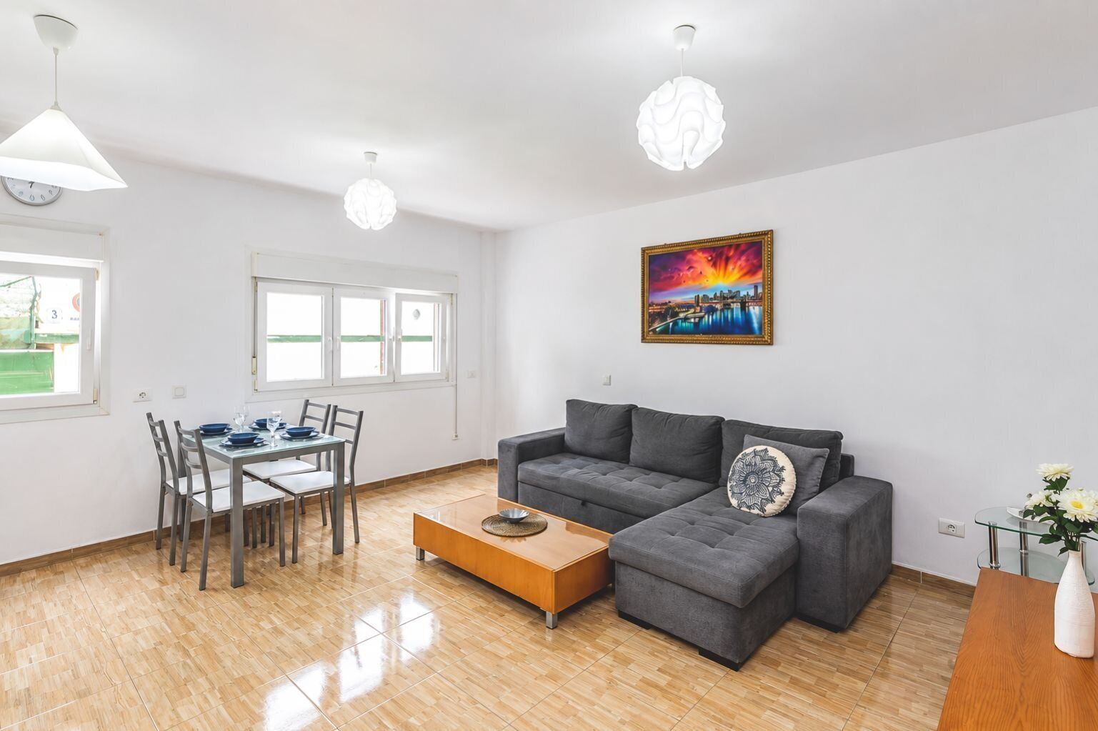 A modern living room with a grey sofa, a wooden coffee table, and a dining area with a table and chairs.