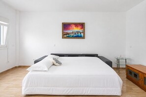 A bedroom with a large bed, a small bedside table, a nightstand, and a painting on the wall. - GuestReady - Bergantín Bañaderos Sea View (Arucas)