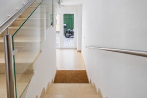 A modern interior with a glass railing, a staircase, and a green door leading to a motorcycle. - GuestReady - Bergantín Bañaderos Sea View (Arucas)