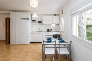 A modern kitchen with white cabinets, a dining table set with blue plates, and a large window. - GuestReady - Bergantín Bañaderos Sea View (Arucas)