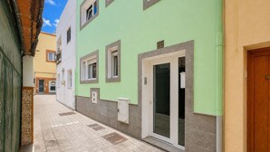 Un estrecho callejón con un edificio de fachada verde, suelo de baldosas y una puerta con ventana.