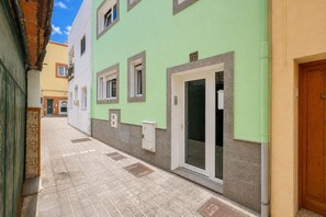 A narrow alleyway with a building featuring a green facade, a tiled floor, and a door with a window. - GuestReady - Bergantín Bañaderos Sea View (Arucas)
