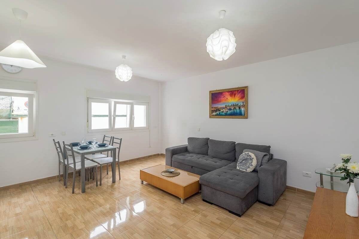 Een moderne woonkamer met een eettafel, een grijze bank en een schilderij aan de muur.