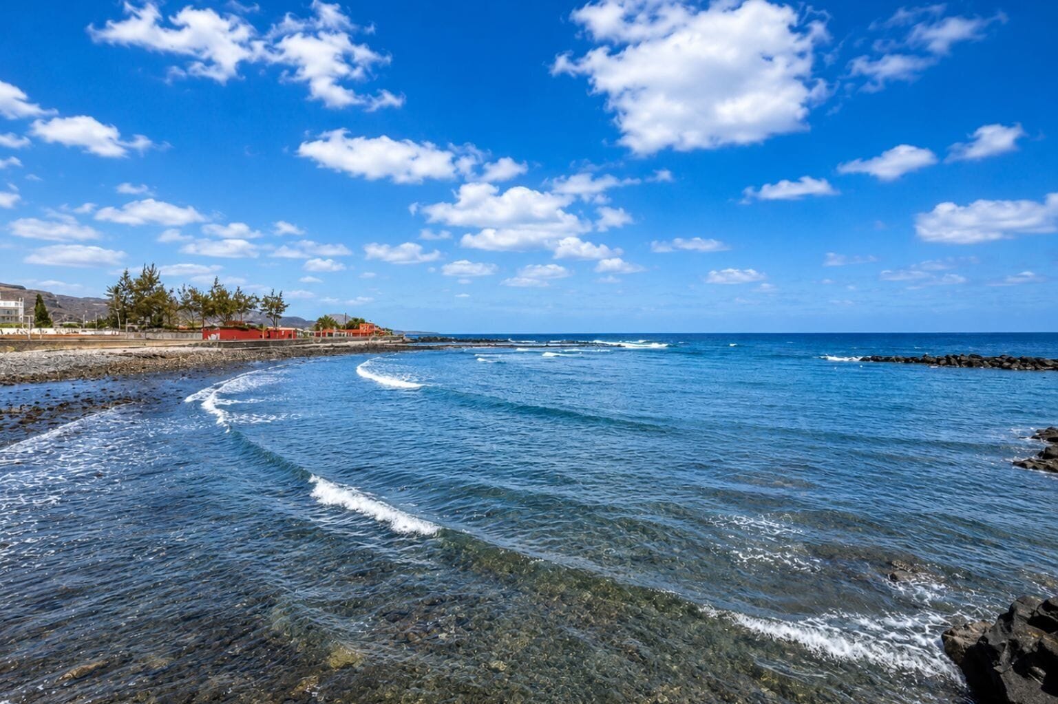 A coastal scene with clear skies, waves, and a rocky shoreline.