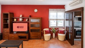 Een woonkamer met een rode muur, een houten tv-meubel, een flatscreen televisie, twee fauteuils, een salontafel en een raam met uitzicht.