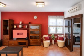 Ein Wohnzimmer mit roter Wand, einer Holz-Unterhaltungsecke, einem Flachbildfernseher, zwei Sesseln, einem Couchtisch und einem Fenster mit Blick.