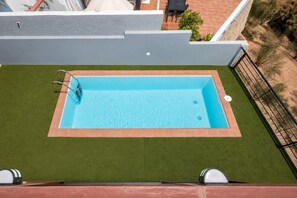 Ein rechteckiger Pool mit Fliesenbordur, umgeben von Kunstrasen, und einer Metallreling an einer Seite.