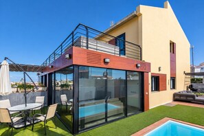 A modern house with a glass-enclosed patio, a pool, and outdoor seating. - GuestReady - Villa Datana with Pool (Mogán)
