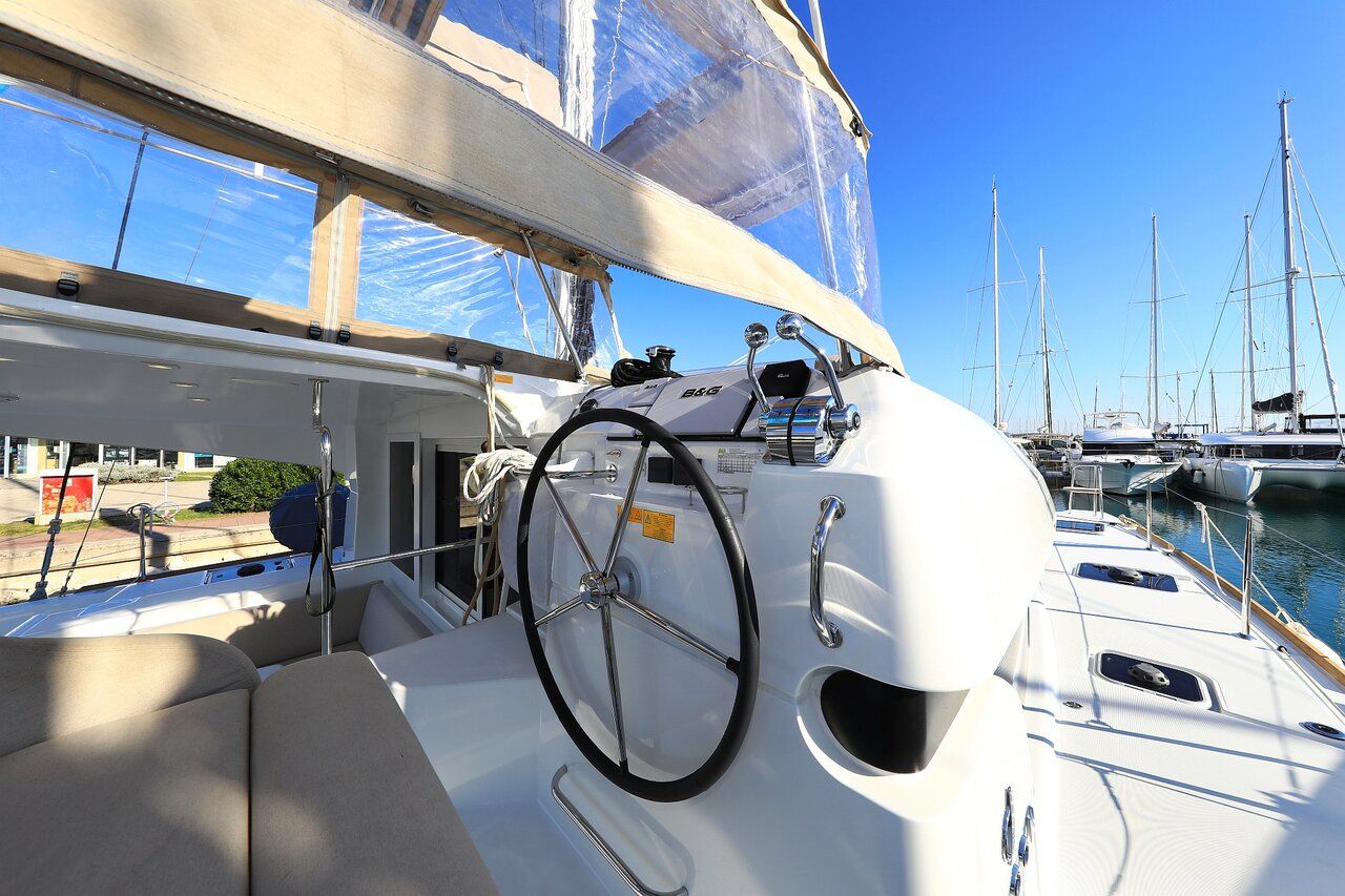 A yacht's deck with a steering wheel, a white cabin, and a view of other yachts docked at a marina.