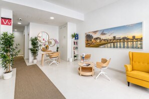 Un espace d’attente moderne agrémenté d’un tableau représentant un paysage urbain, d’un comptoir d’accueil, de sièges et de plantes en pot.