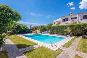 A rectangular swimming pool with a metal ladder, surrounded by a well-maintained lawn and stone pathways. - GuestReady - Tarantos Sea View and Pool (Playa del Ingles)