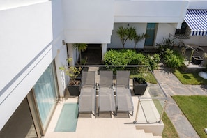 A modern outdoor seating area with a glass balustrade, potted plants, and a stone pathway leading to a building entrance. - GuestReady - Tarantos Sea View and Pool (Playa del Ingles)
