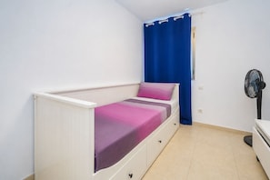 A single-bed room with a white headboard, a bedside table, a fan, and a blue curtain. - GuestReady - Tarantos Sea View and Pool (Playa del Ingles)