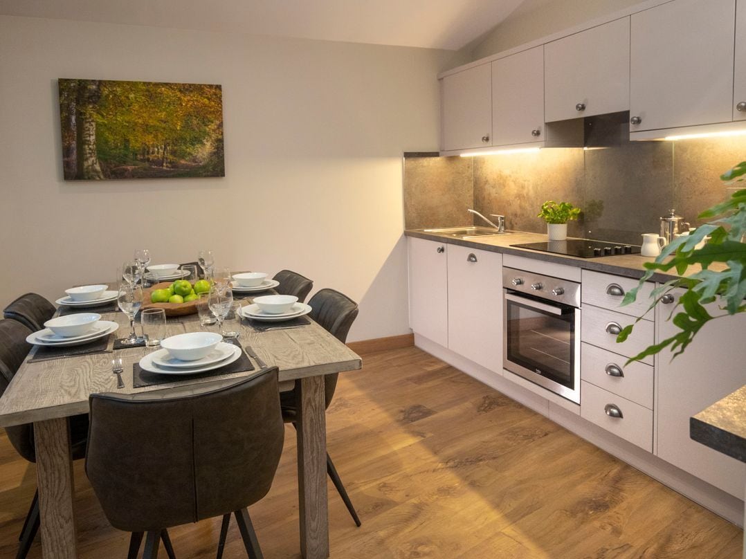 Una cocina moderna con armarios blancos, una mesa de comedor de madera y un cuadro en la pared.