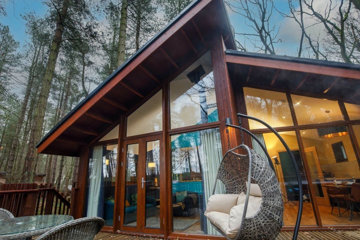A modern cabin with a glass door entrance, a hanging chair, and a wooden deck.