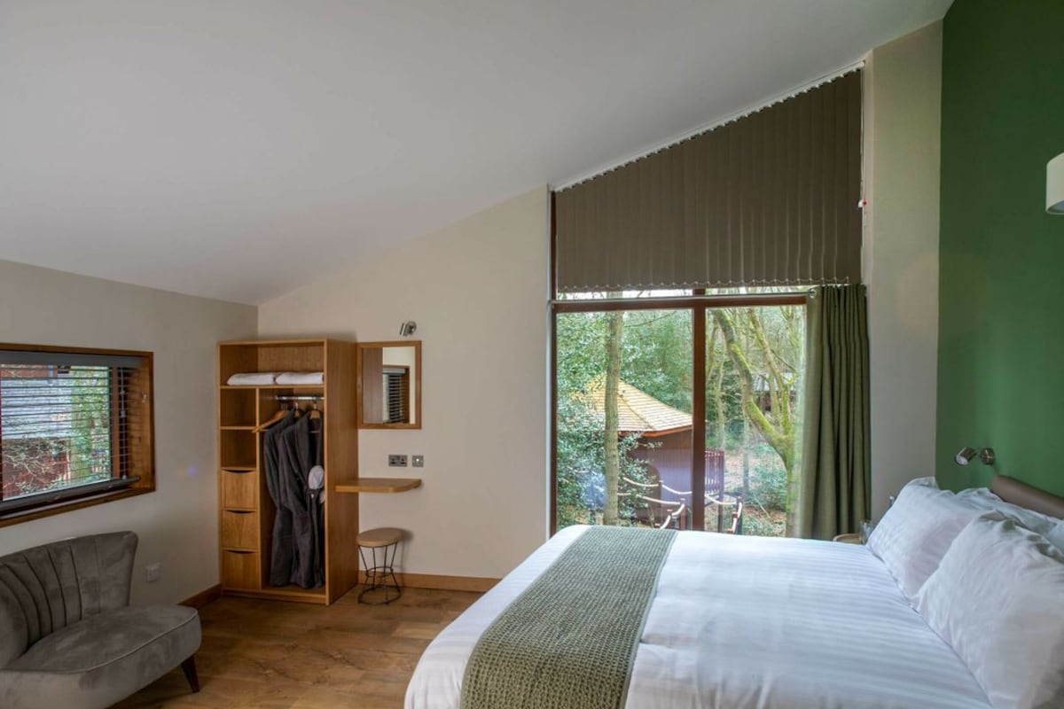 A bedroom with a bed, a chair, a wardrobe, and a window with a view of trees.