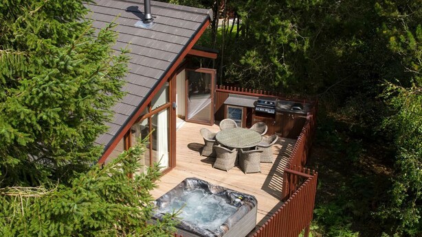 A hot tub on a deck with outdoor furniture, surrounded by a wooden fence and dense greenery.