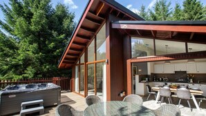 A modern outdoor deck with a hot tub, dining area, and kitchen.
