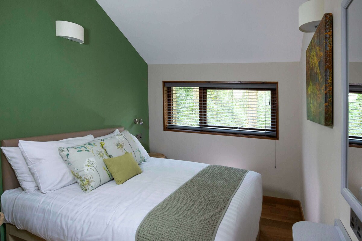 A bedroom with a bed, a window with blinds, a green wall, and a painting.