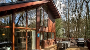 A wooden cabin with a hot tub, deck, and outdoor grill.