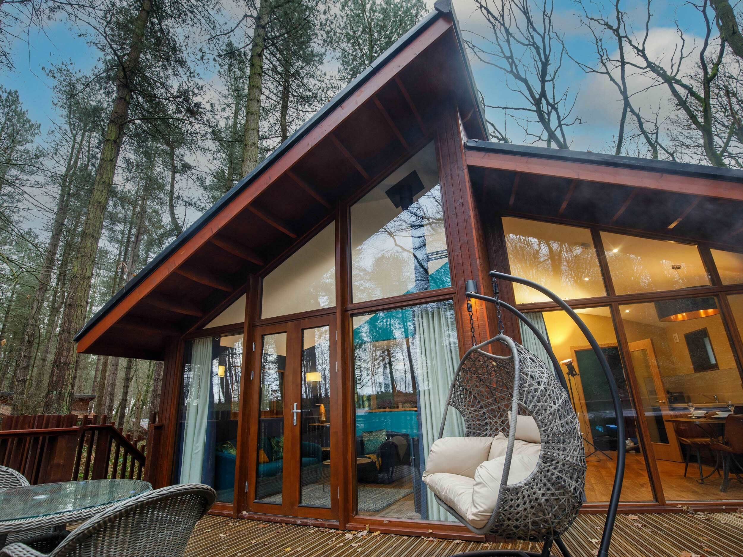 A modern cabin with large glass doors, a hanging chair, and a dining area.
