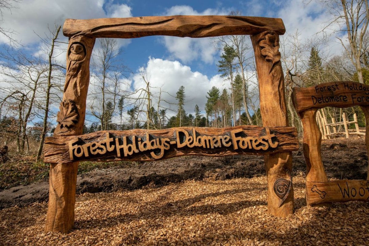 A wooden sign with carved details and text indicating 'Forest Holidays - Delamere Forest.'