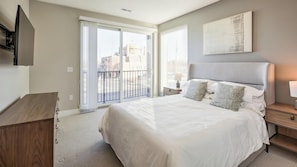 A bedroom with a bed, a TV mounted on the wall, a window with blinds, and a view of the outside. - Landing Amazing 1bd, Game Room, Gym (Salt Lake City)