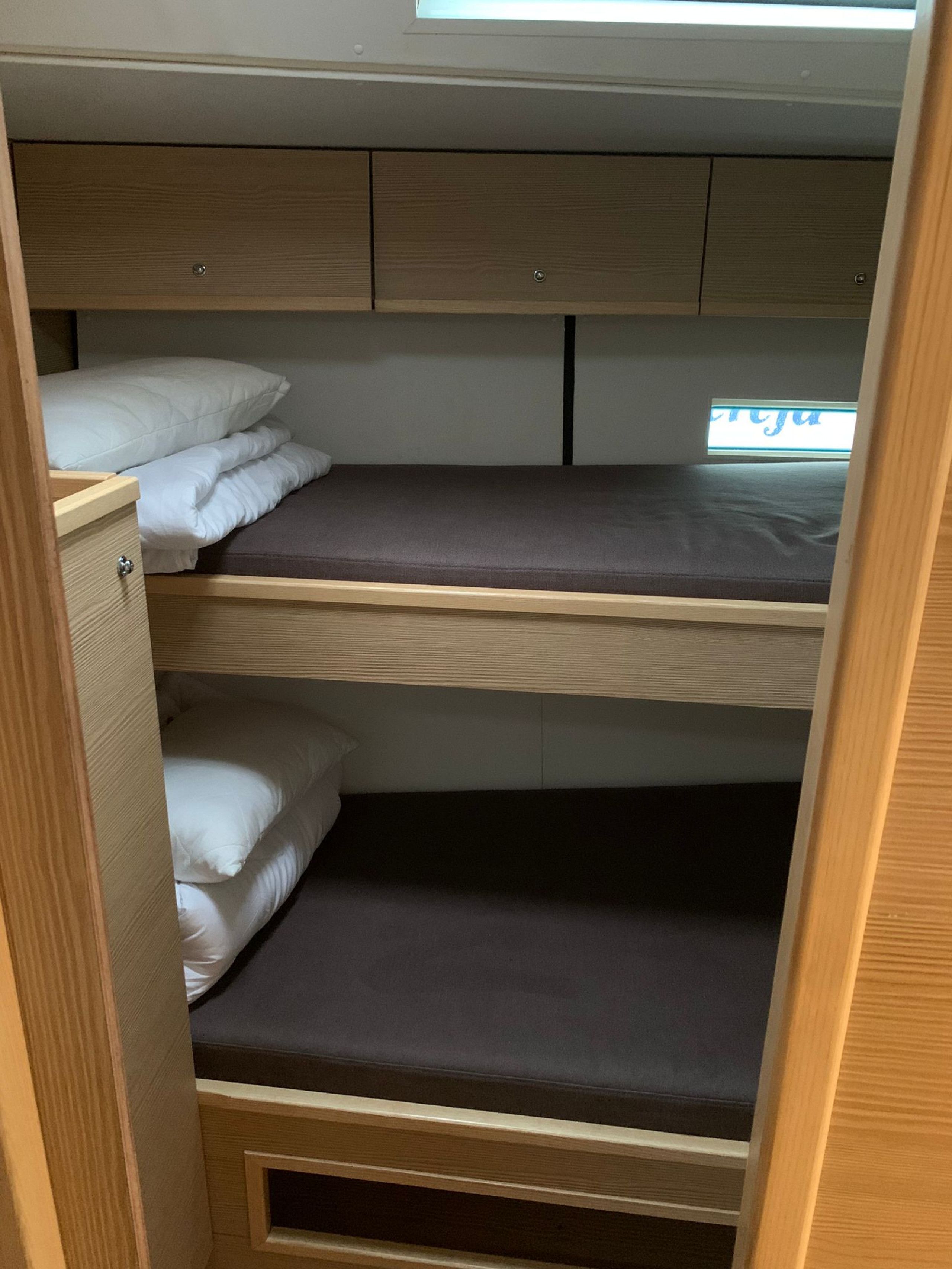 A bunk bed with a wooden headboard, a lower bunk with a dark mattress, and a top bunk with a light-colored mattress.