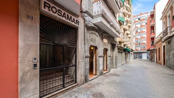 Una calle estrecha con un edificio identificado como 'ROSAMAR' a la izquierda, que presenta una gran puerta metálica y una entrada pequeña.