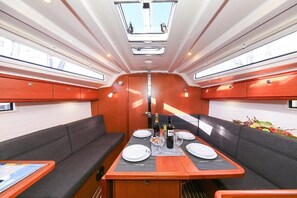 Interior de barco con zona de comedor, asientos acolchados y una mesa central dispuesta para una comida.