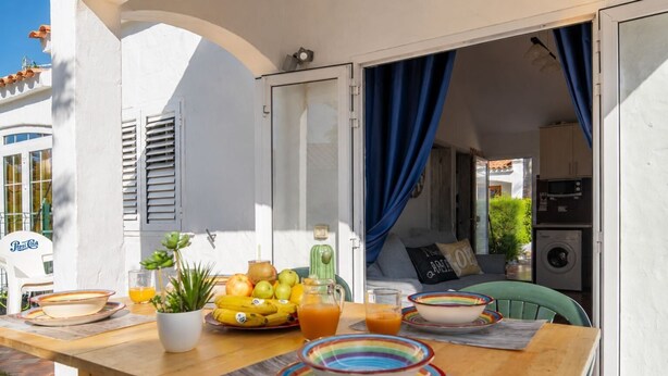 An outdoor dining area with a wooden table, various dishes, and a view of the interior. - GuestReady - Los Arcos Outdoor Oasis (San Bartolomé de Tirajana)