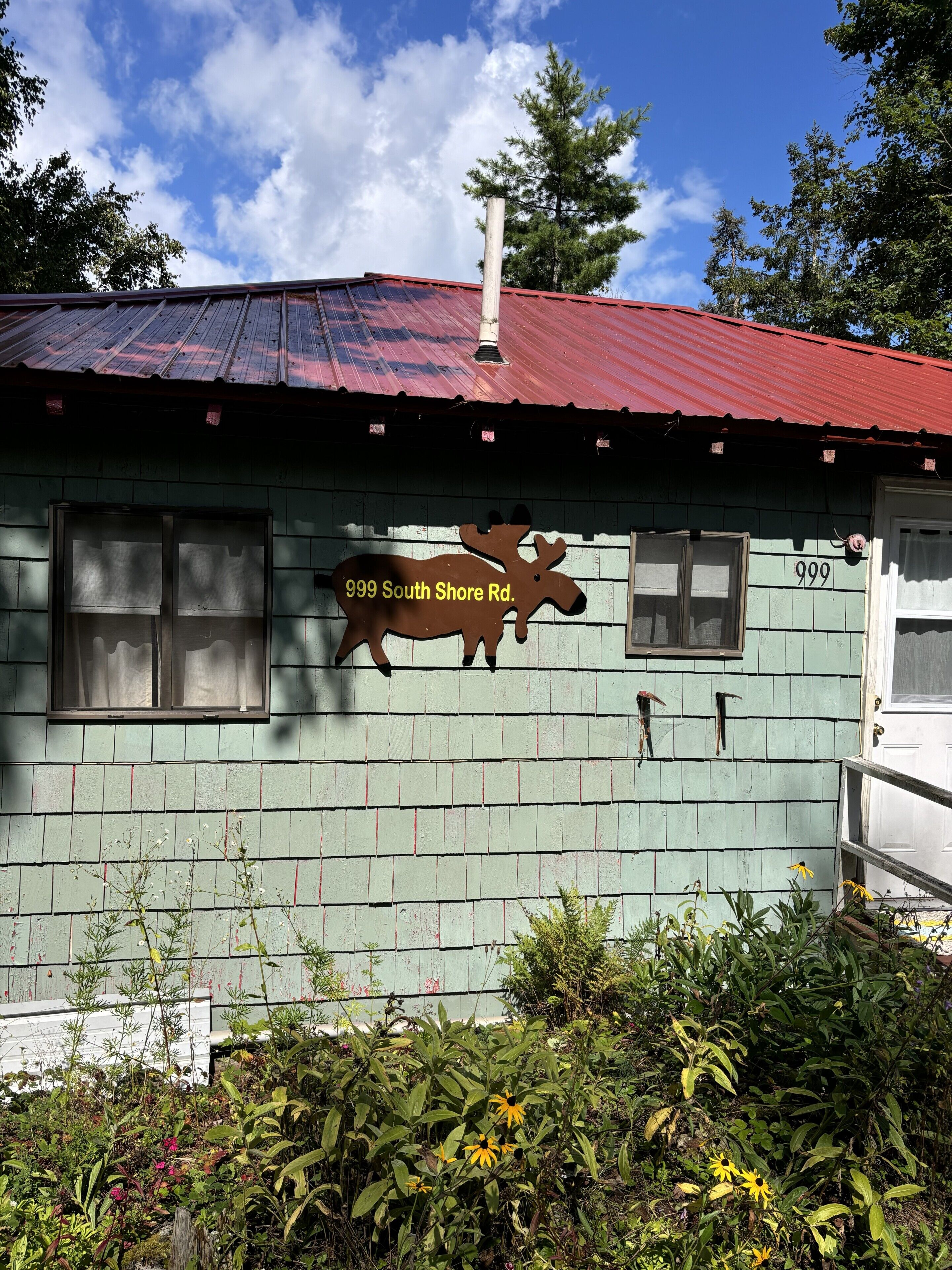 A rustic building with a green exterior, a red roof, and a sign indicating '999 South Shore Rd.'