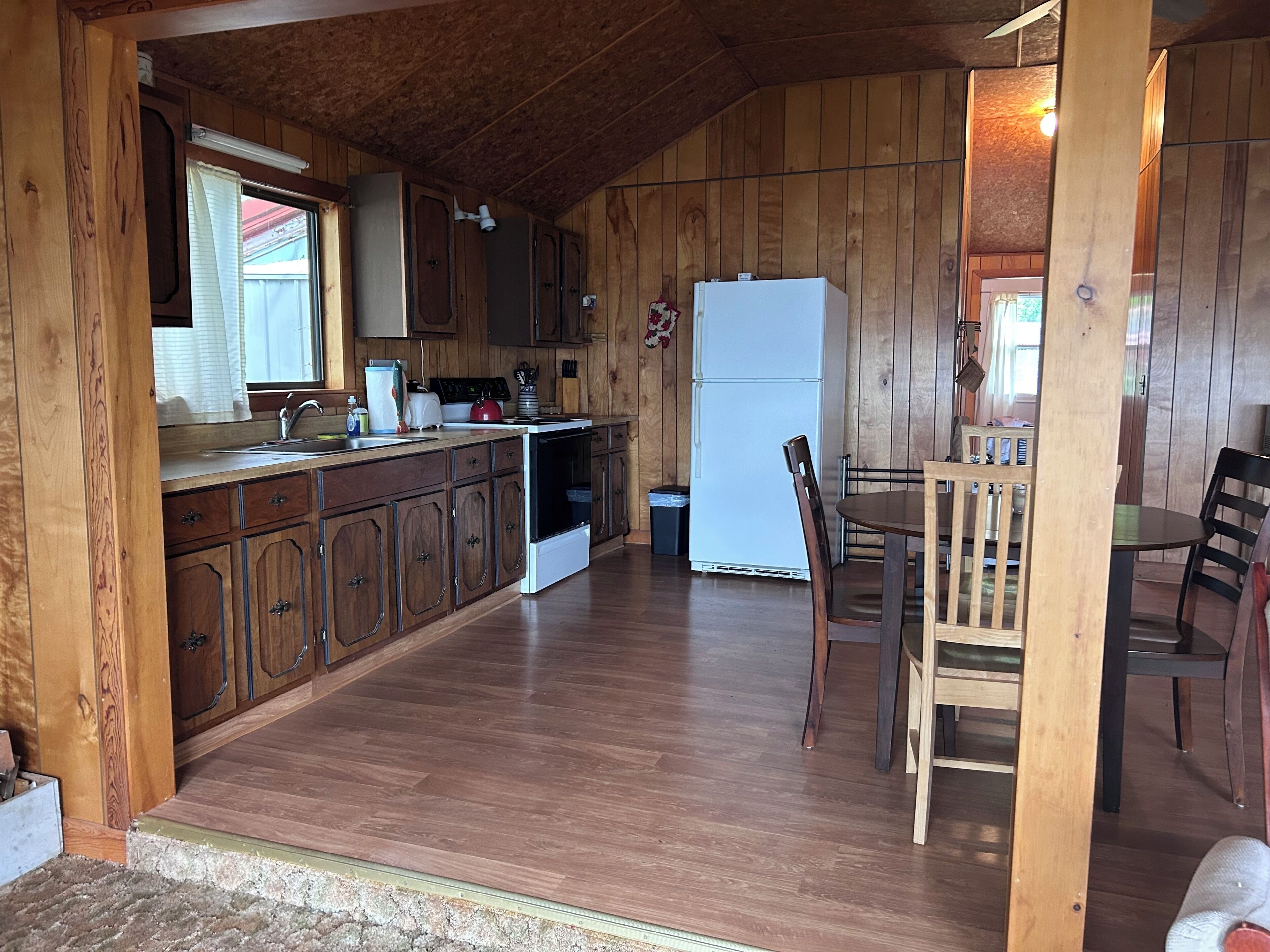 A wooden cabin interior with a kitchen, dining area, and a small living space.