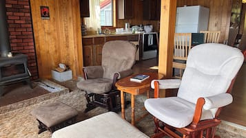 A cozy cabin interior with a fireplace, wooden furniture, a kitchen area, and a window with curtains.
