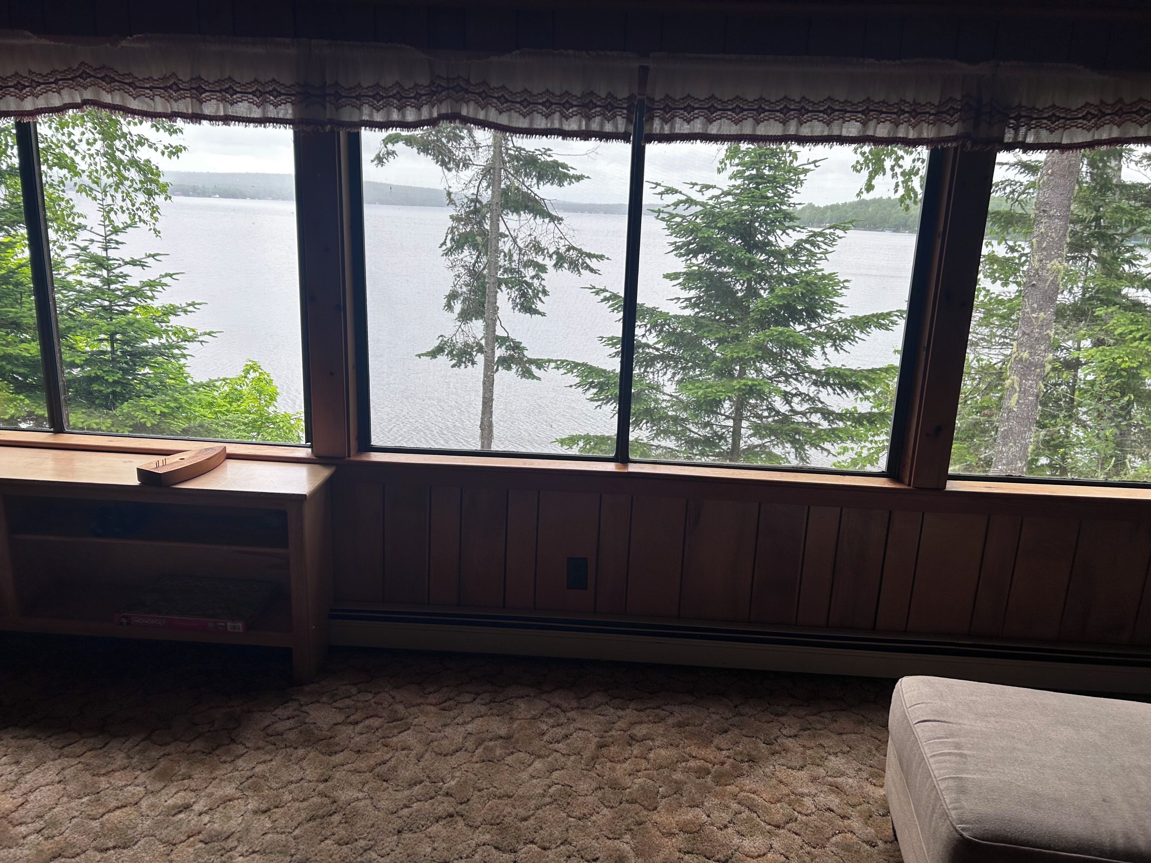 A room with a large window overlooking a lake, a wooden bench, and a carpeted floor.