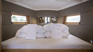 Un letto rifatto con lenzuola e cuscini bianchi, due finestre con vista sugli edifici e un soffitto con faretti.