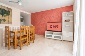 A room with a dining table and chairs, a television on a stand, and a white shelving unit. - GuestReady - Modern Retreat with Pool (Caleta de Fuste)