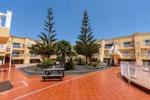 A courtyard with a tiled floor, a picnic table, and two tall trees. - GuestReady - Modern Retreat with Pool (Caleta de Fuste)
