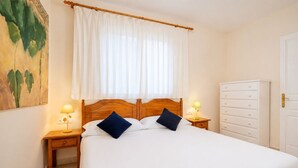 Una habitación de hotel con una cama grande, dos mesitas de noche con lámparas, un cabecero de madera, un armario blanco y un cuadro en la pared.