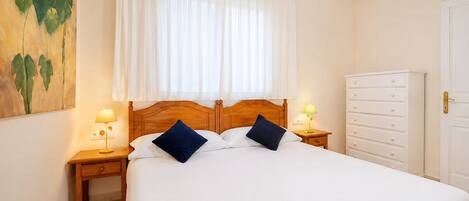Une chambre d’hôtel avec un grand lit, deux tables de chevet avec des lampes, une tête de lit en bois, une armoire blanche et un tableau au mur.