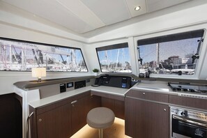 Interior de barco com painel de controle, janelas, um banquinho e um fogão.