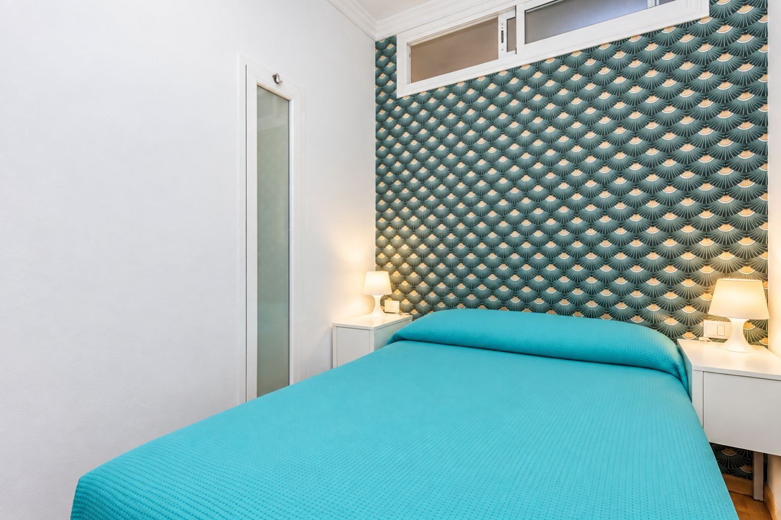 Una camera da letto con un letto, un comodino, una lampada e una parete decorata.