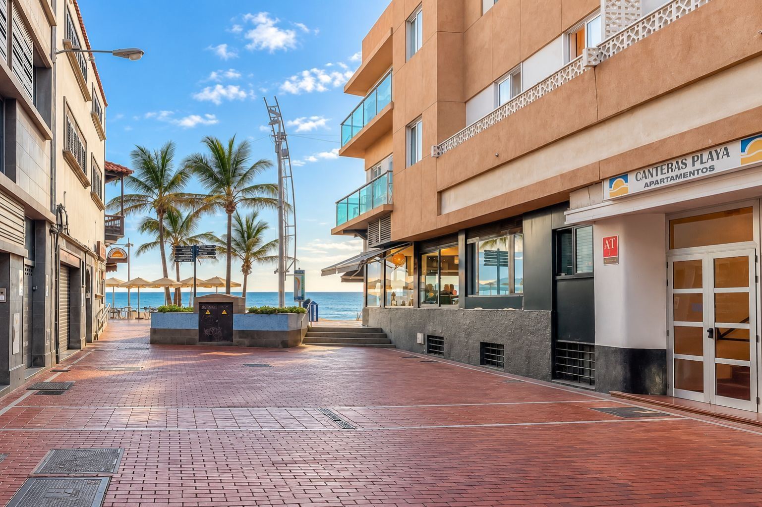 A beachfront property with a paved walkway, palm trees, and a building labeled 'Canteras Playa Apartamentos.'